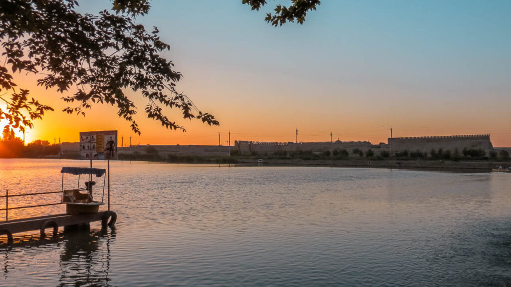 El lago de Bukhara cerca del Mausoleo de Ismail Somoni al atardecer. Se lo ve lleno de agua, con la muralla de la ciudad por detrás.